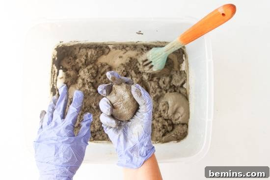 Man with gloves in hands is holding a piece of mud from a box of mud and spoon.