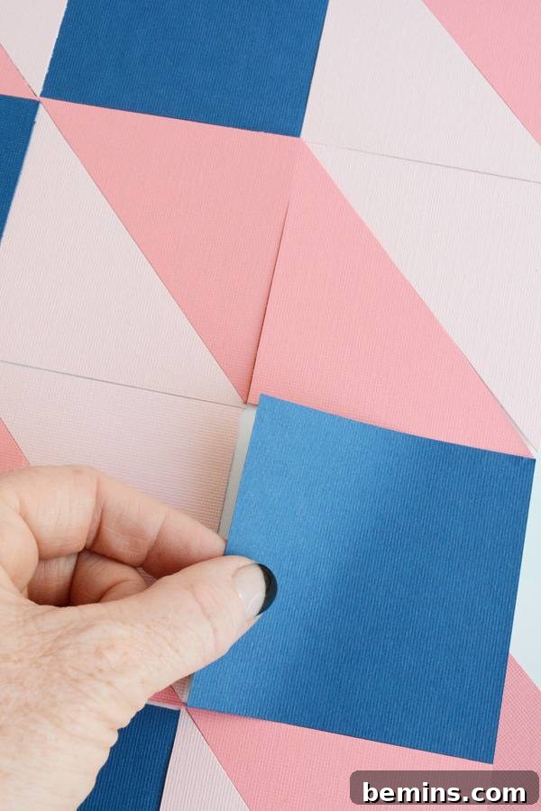 A hand hold a square blue piece of paper above pink and white pieces of square paper.