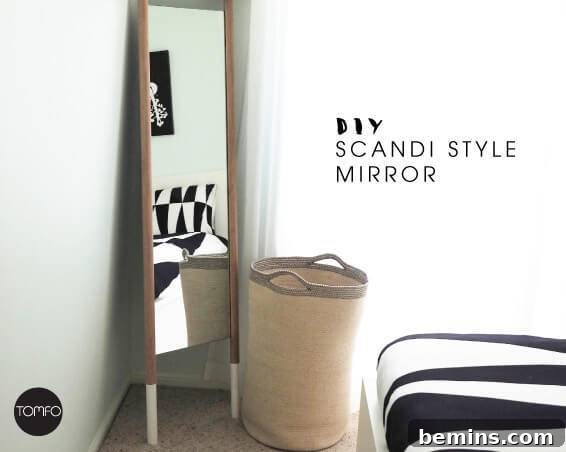 Scandi style mirror resting up against a wall in front of a small clothes hamper in a bedroom