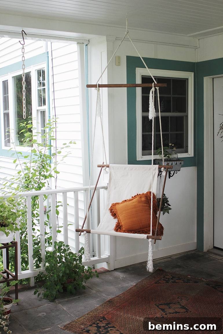 A swing on the porch of a house with white paint and green trim