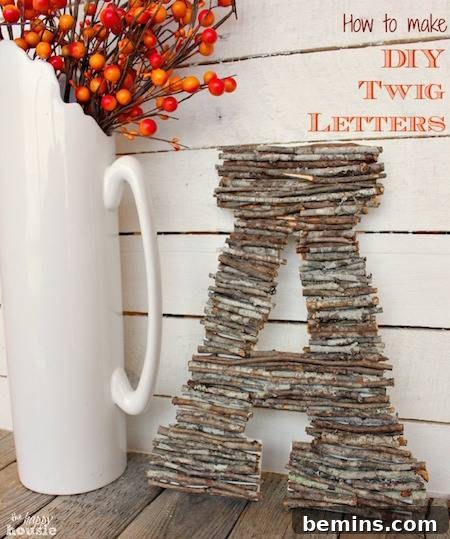 A letter 'A' crafted from natural twigs, displayed near a vase of vibrant red flowers.
