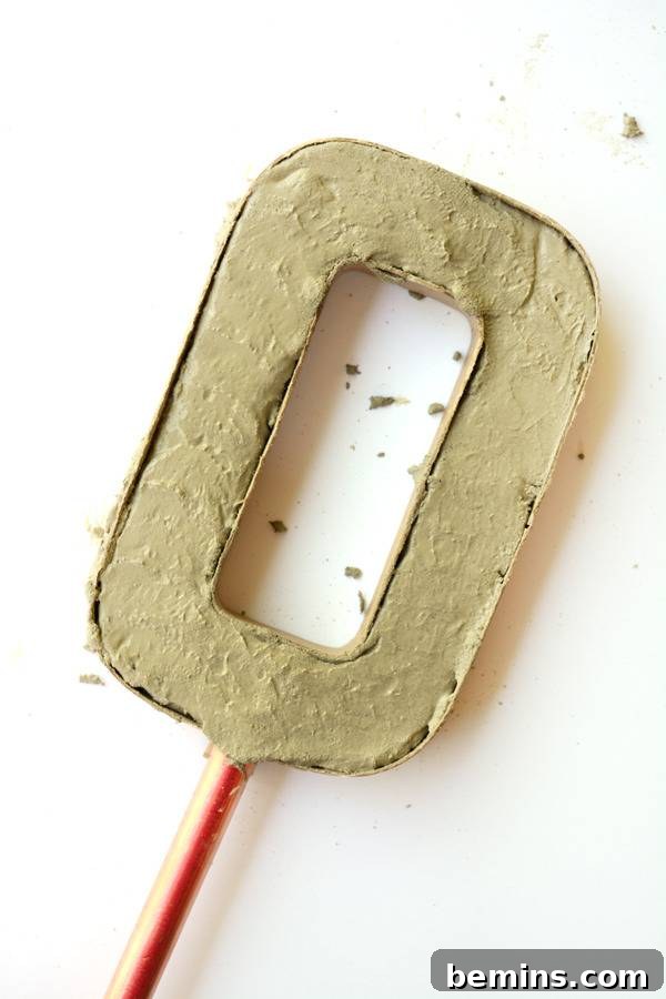 A concrete letter 'O' on a copper stick, partially cured, after being removed from its mold, showcasing the early stage of the drying process.