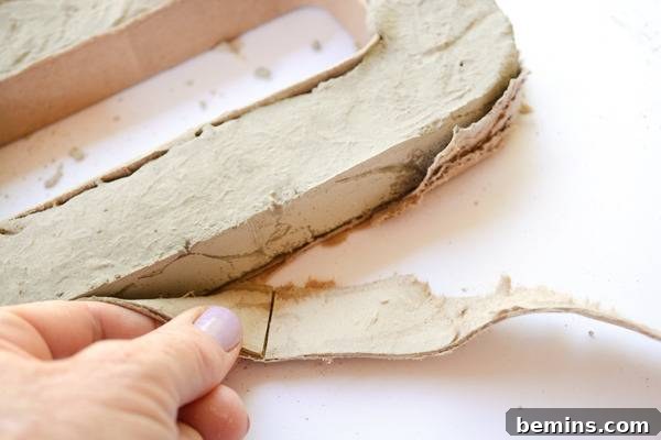 A person carefully pulling the cardboard mold away from a partially set concrete letter, revealing its form.
