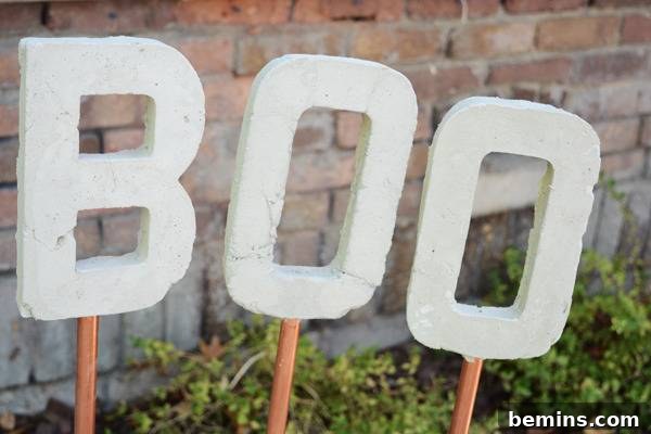 The capital letters B, O, O, each on a copper stick, leaning against a red brick wall, showcasing the finished Halloween garden stakes.