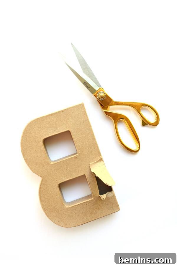 An upside down cardboard letter B with a chunk removed, placed next to a pair of gold scissors, ready for crafting.
