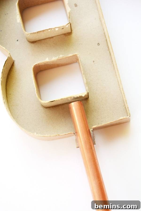 A prepared mold for making a concrete letter B, showing the precisely cut opening at the base for the pipe insertion.