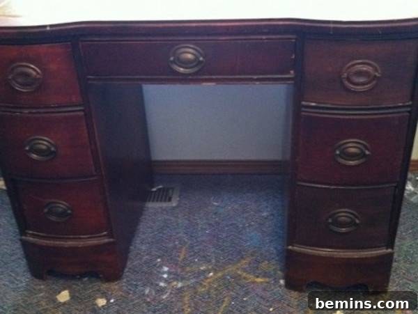 A dark brown desk with oval worn brass drawer handles.