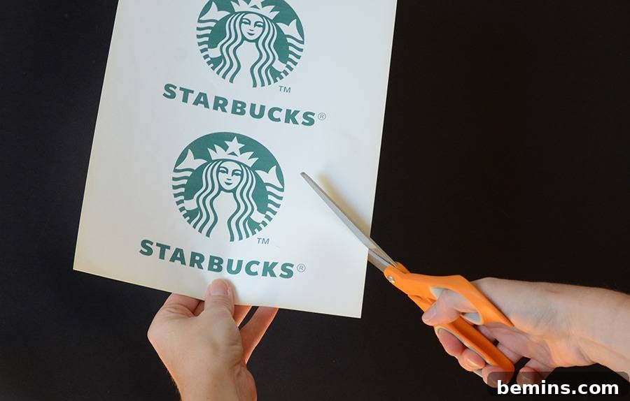 Close-up of a hand cutting out a printed Starbucks logo with orange scissors.