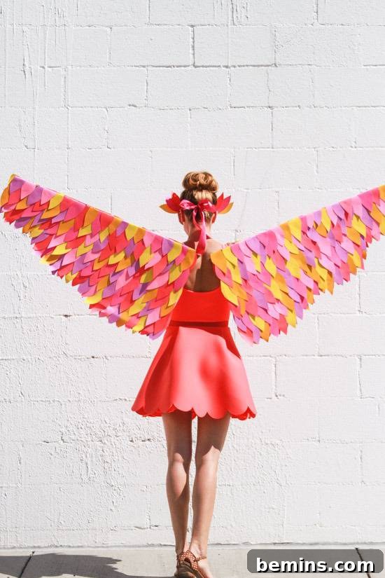 Craft Your Own Bird Costume: A Step-by-Step Guide 10 The back of a woman with orange,pink, purple and yellow wings spread and an orange skirt standing in front of a white stone wall.