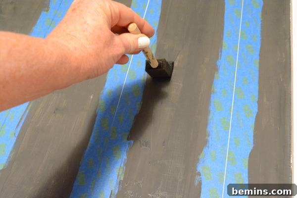 A person is painting grey stripes with a blue and green pattern.