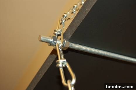 Metal chain attached to a screw on a rod that is attached to a wooden board.