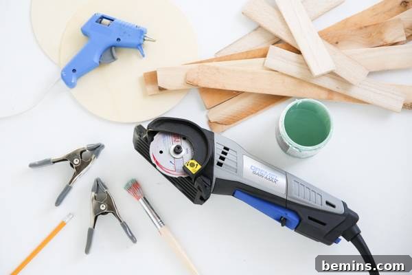 An assortment of crafting tools including a cutter, clips, glue gun, paint brushes, paint bottle, and wooden sticks are arranged on a table.