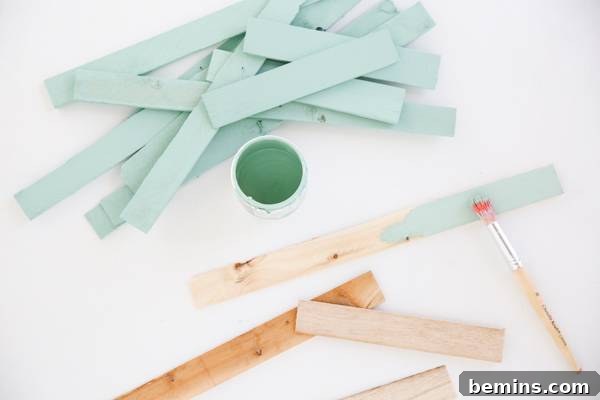 A light blue paint bottle, painted and unpainted wooden sticks, and a paint brush are displayed.