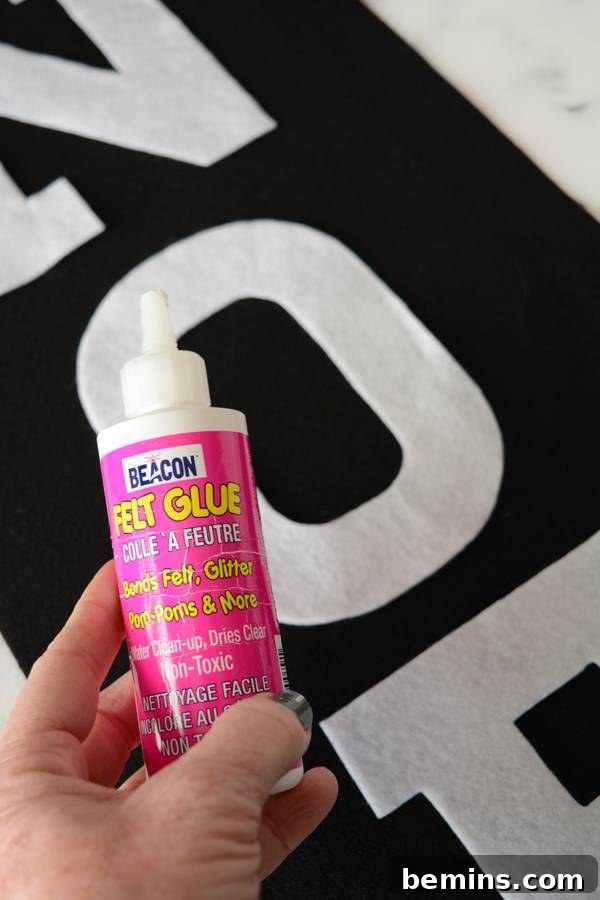 A hand holding a bottle of felt glue, ready to adhere the letters to the banner.