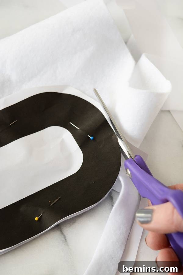 Cutting the white felt with a pinned pattern attached, demonstrating the cutting process.
