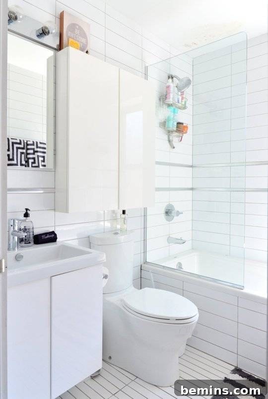 A white tiled bathroom with a cabinet above the toilet.