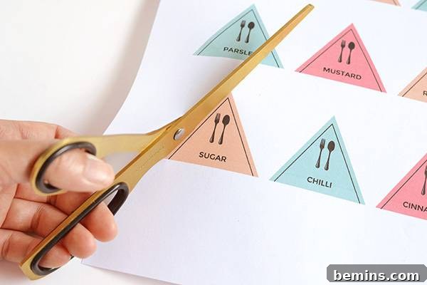 A person's hands holding scissors, carefully cutting out rectangular label designs from a printed sheet of paper.