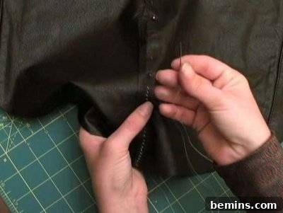 A needle and thread being used to sew black leather.