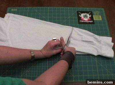 A hand holding a scissor cutting the sleeve of a dress shirt.