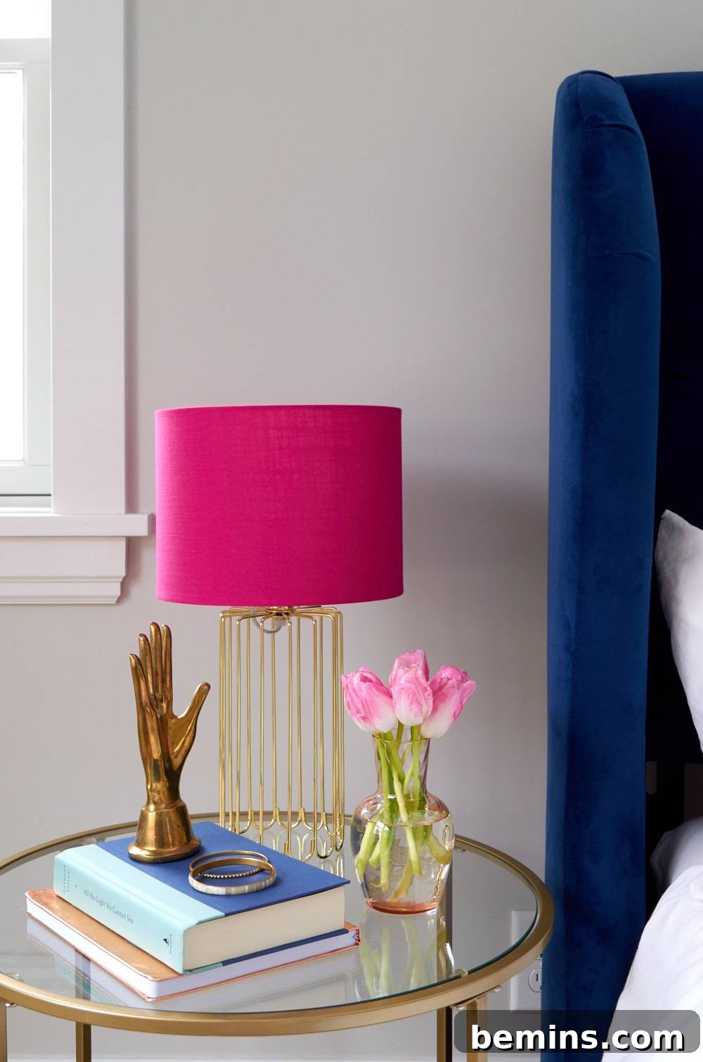 Pink lamp on a nightstand with books and accessories