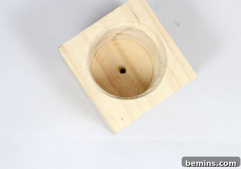 A cleanly drilled round cavity sits within a square block of wood, ready for a small drainage hole.
