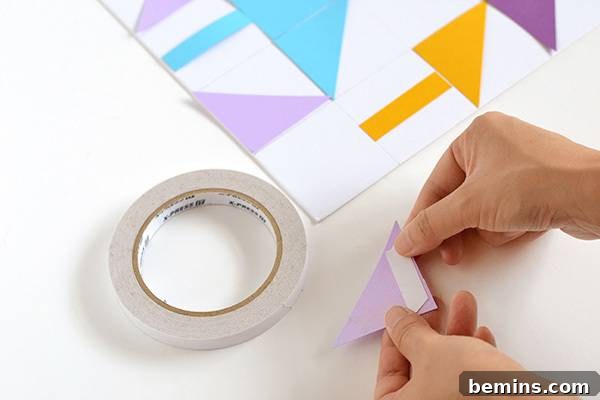 Hands carefully applying glue to the back of a colored paper triangle before sticking it onto the grid