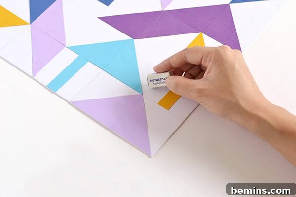 A hand gently erasing faint pencil grid lines from the finished geometric paper art with an eraser