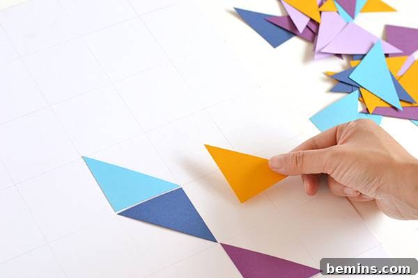 Hands arranging cut paper shapes within the grid lines on a white card, experimenting with design