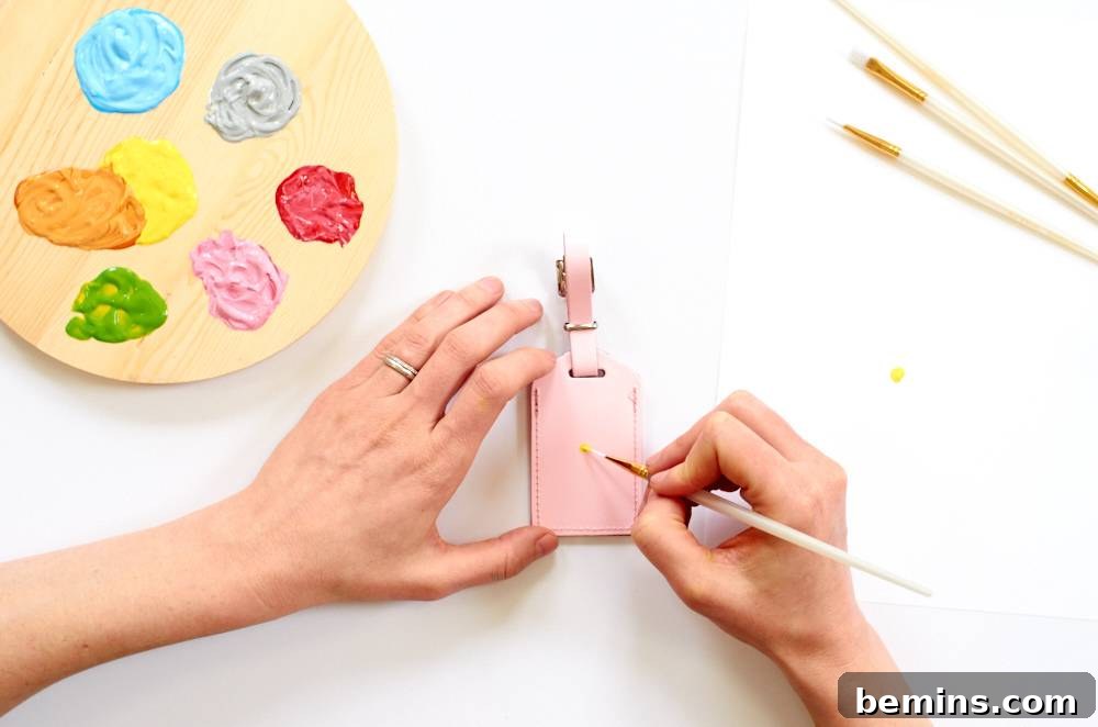Two hands are painting an object next to paint and brushes. Sketch out your designs or gather inspiration before you start painting your leather luggage tags.