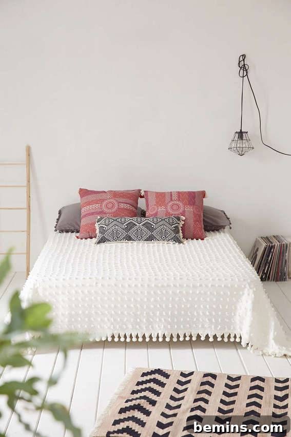 A white room with a made bed that has two red pillows and a white cover and a tan rug with brown chevrons on the floor.
