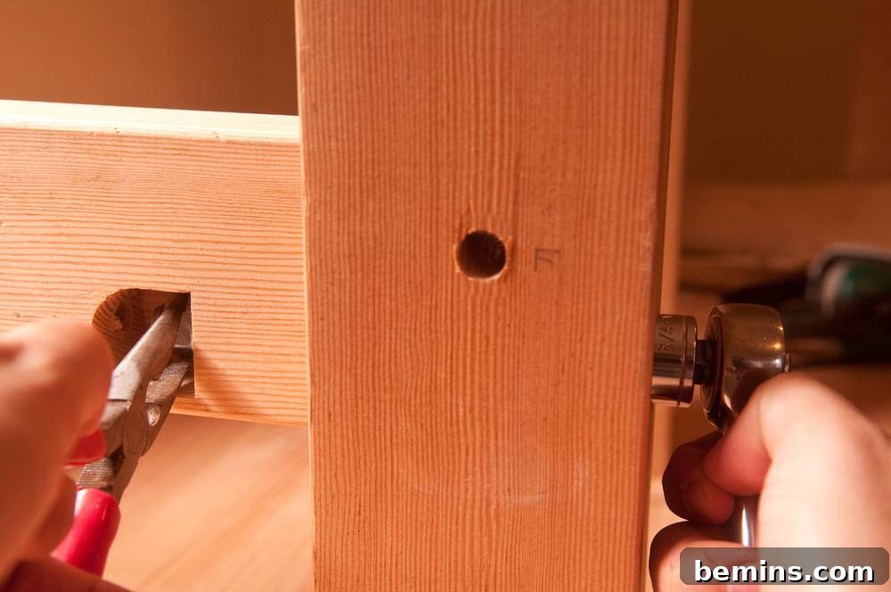 A person drilling a hole with a playa and a wrench in the wooden bench.