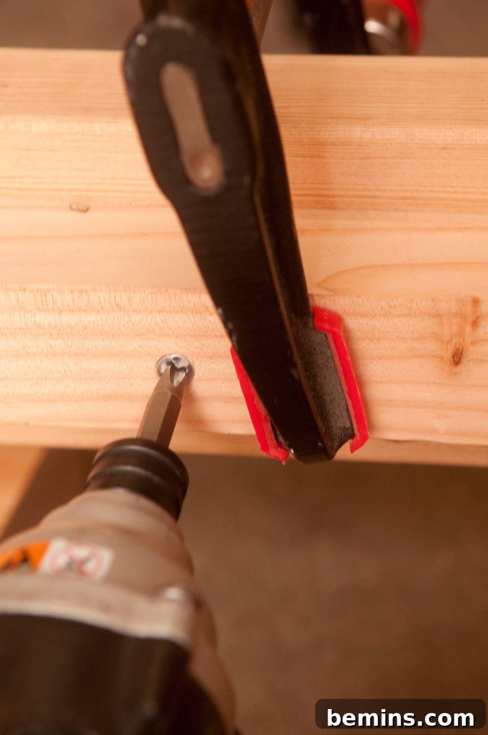 A drill head going into a screw on a board that is in a clamp.