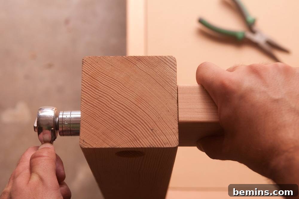 One hand using a tightening tool while the other grasps a piece of wood held next to a square upright beam.