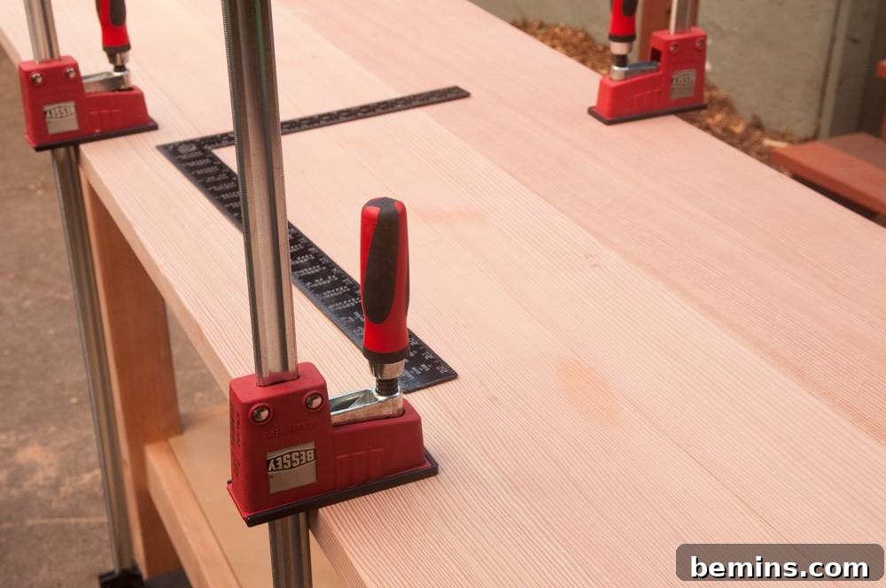 A red clamping device is holding a silver pole to a wooden surface.
