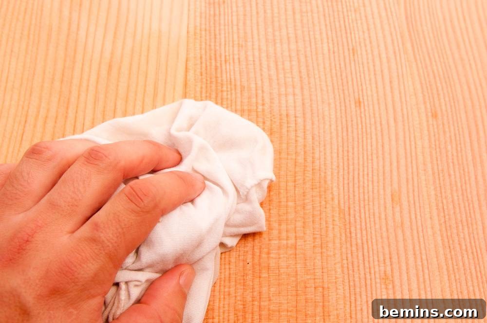 A hand holding a crumpled white rag is resting on a light wooden surface.