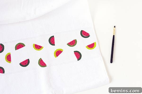 A paint brush lying near a white cloth on which watermelons are printed.