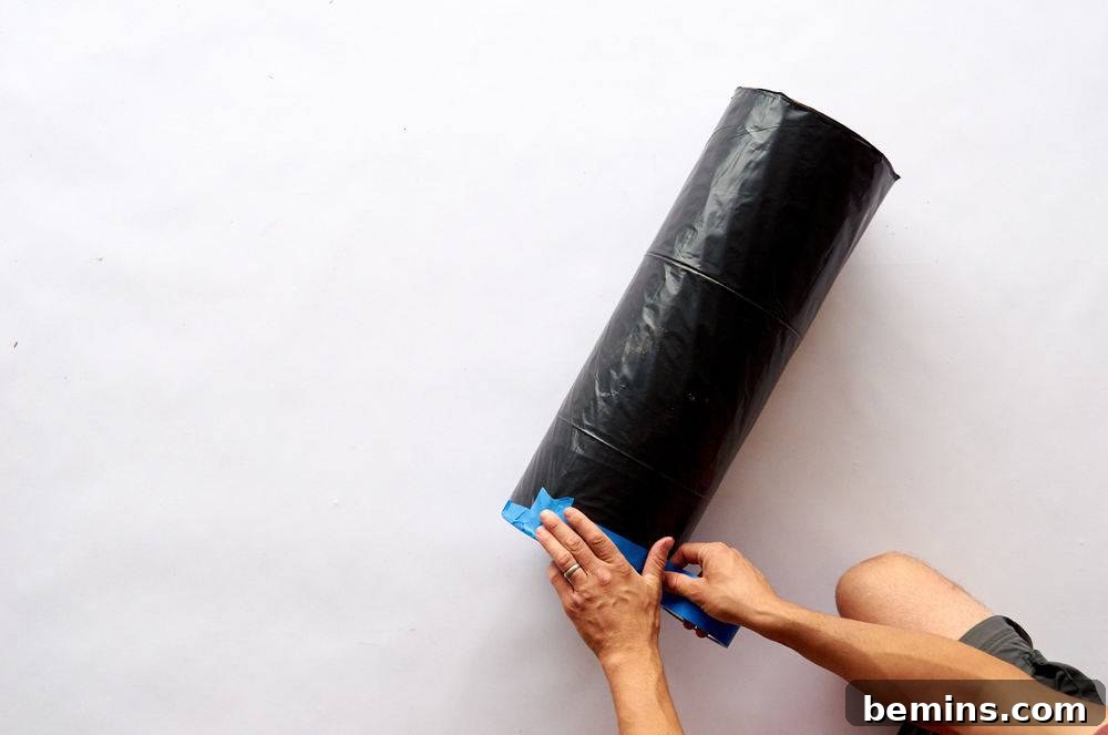 A pair of man hands taping a roll of black plastic with blue tape.