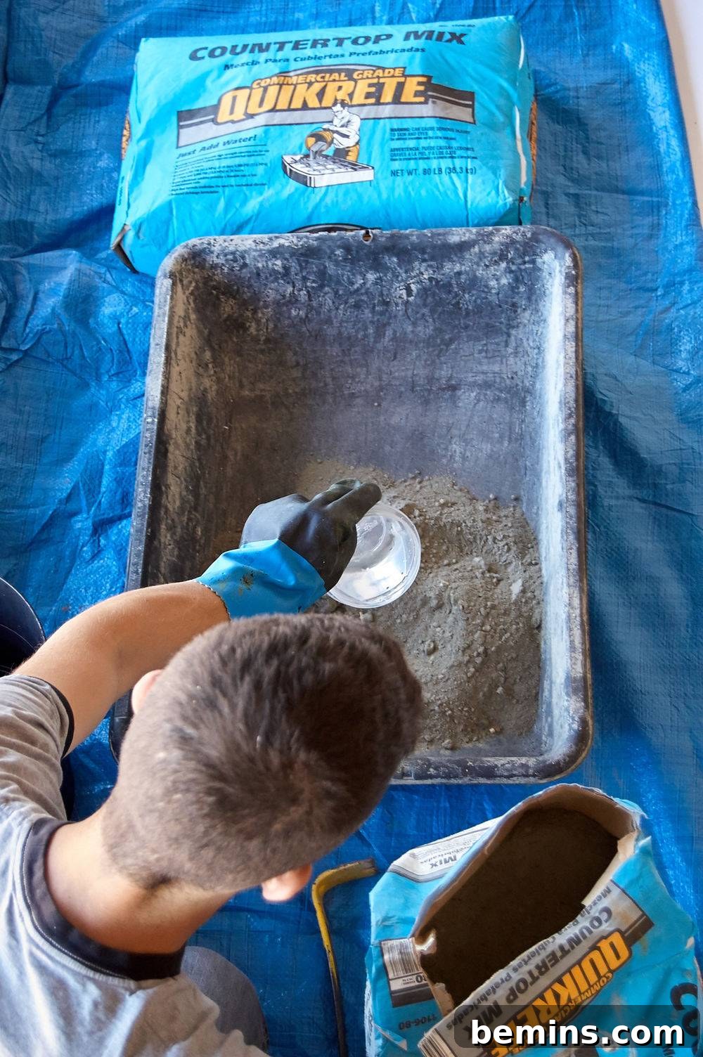 A man mixing commercial grade concrete with water in a rectangular box