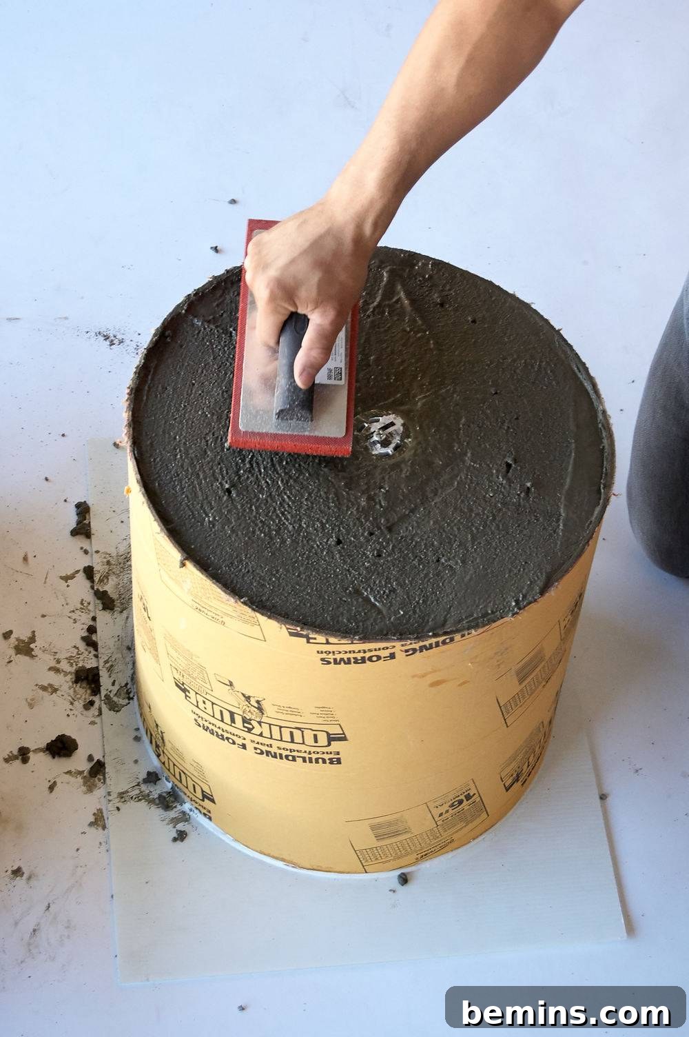 A person uses a trowel to flatten the surface and smooth the surface of concrete in a large container.
