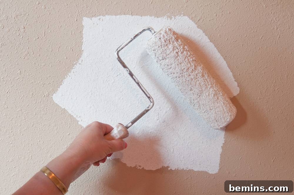 A person using a paint roller to apply white paint to a tan wall.
