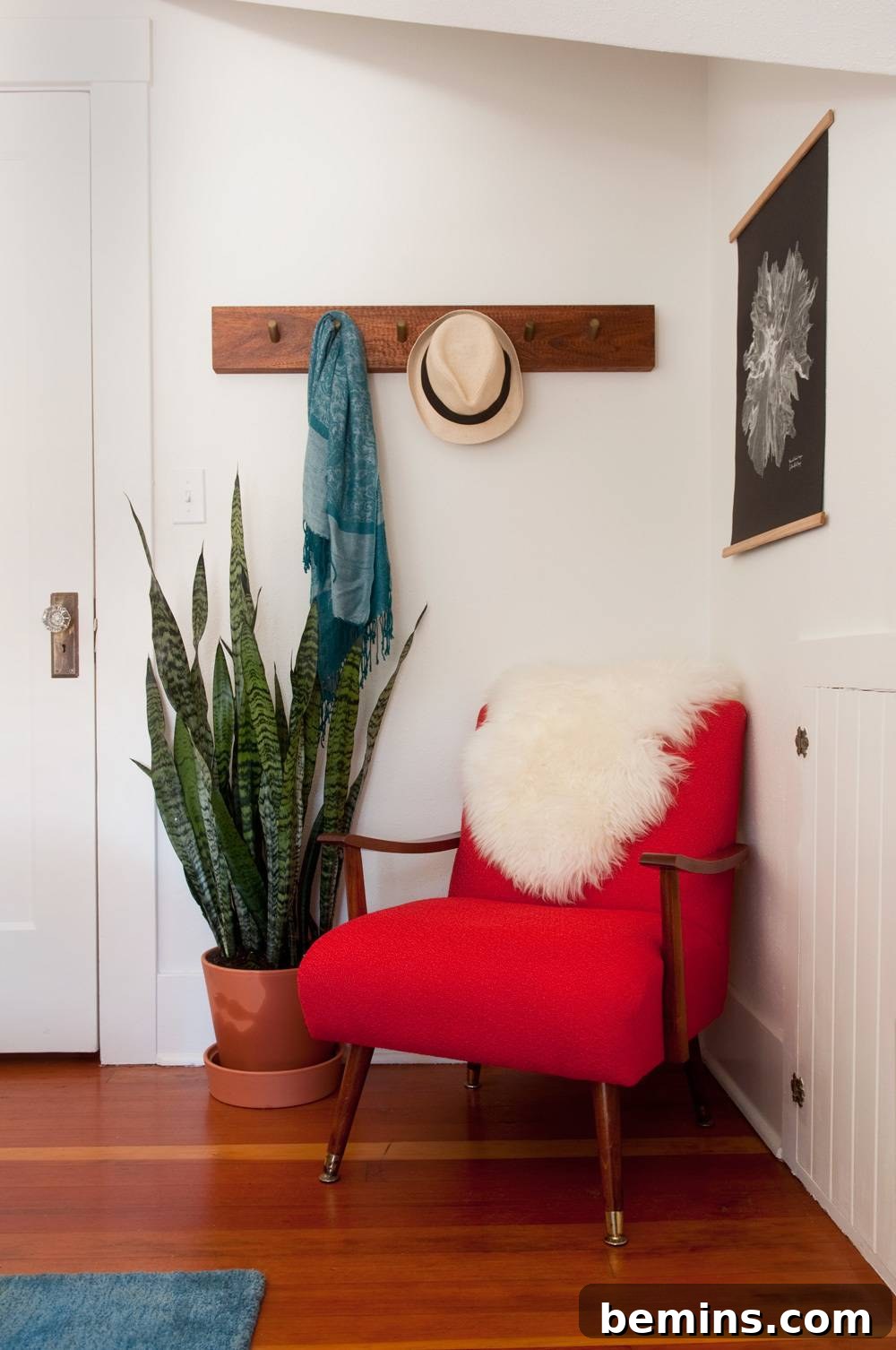 A red chair sits in the corner of a room next to a plant.