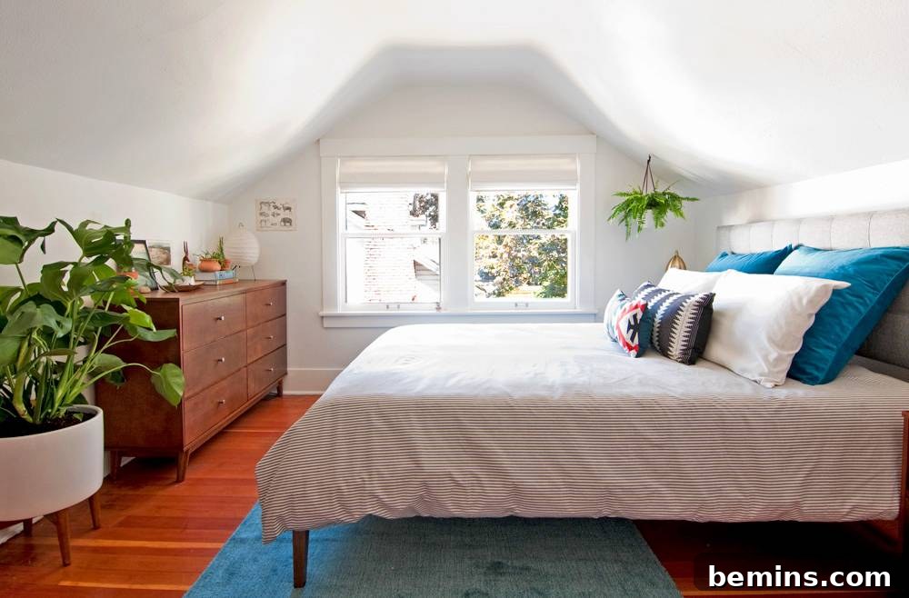 A bed with white sheets and blue and white pillows stands in a room with wooden floors and sloping ceilings.