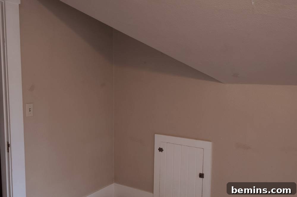 A beige wall and ceiling meet a white door leading to the unfinished attic space.