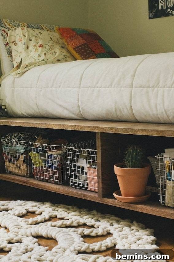 A made bed on a wooden frame with a shelf underneath containing a potted plant and three wire baskets.
