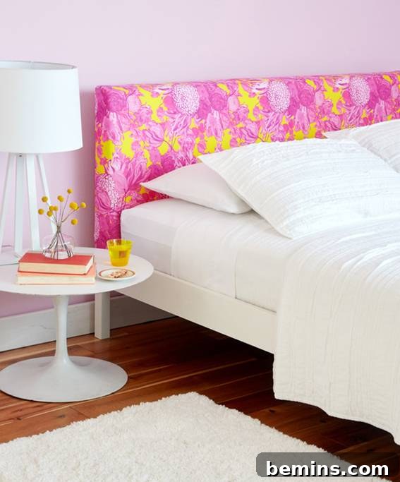 A white bed with a pink and yellow headboard and a nightstand next to it.