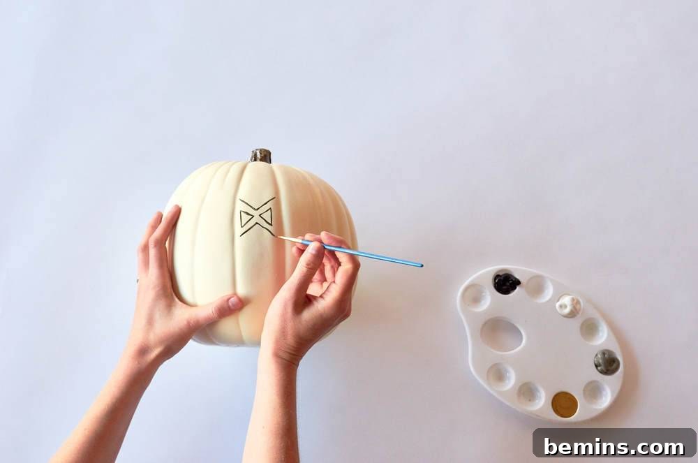 A person is drawing on pumpkin using paint brush.