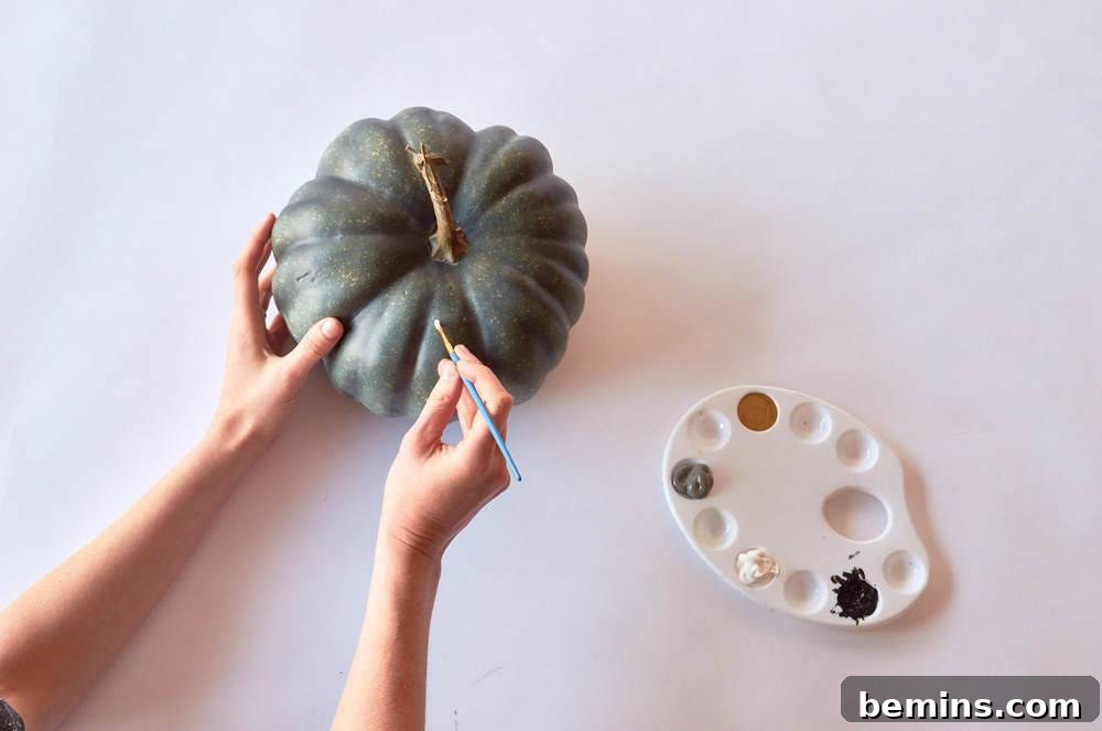 A woman painting a pumpkin with gray paint.