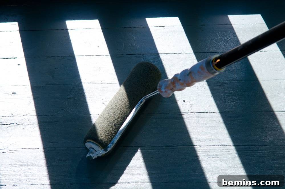 Person using a roller to apply paint to a wooden porch deck.