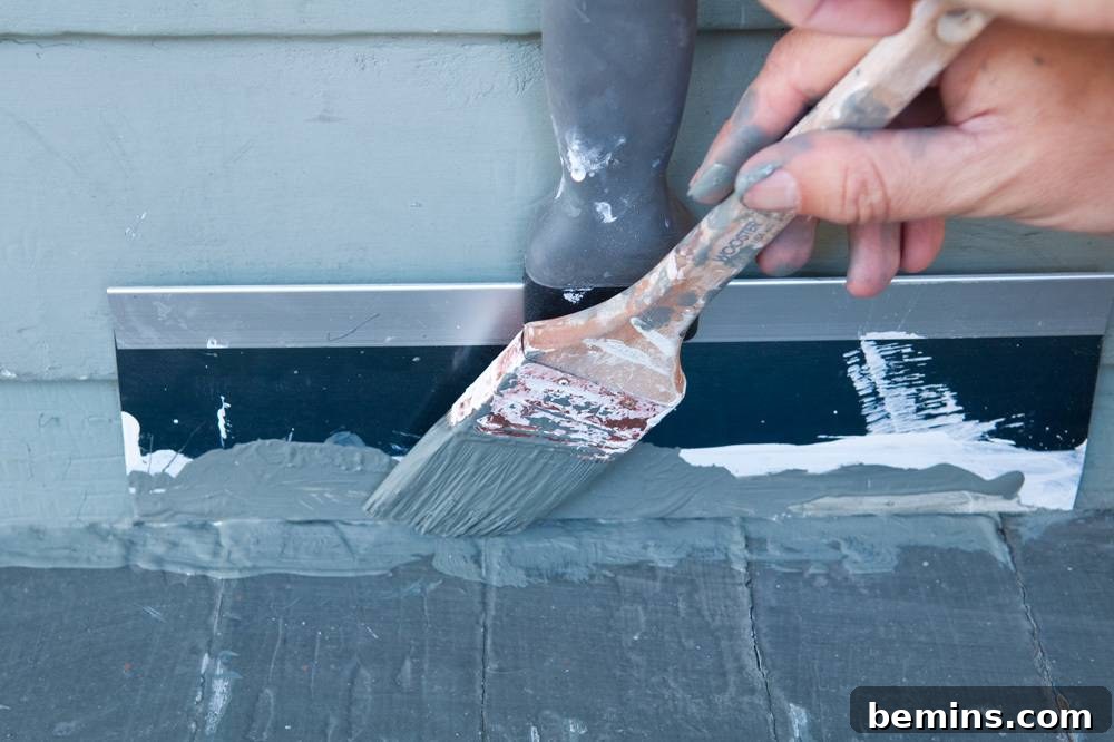 Person applying gray paint to a baseboard with a brush.