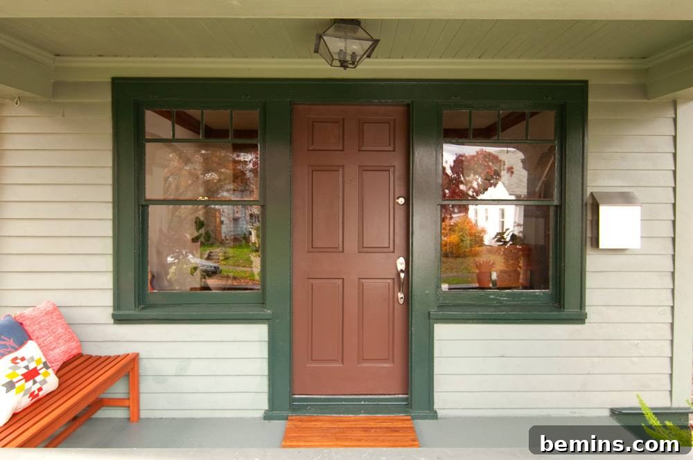 House with a brown wooden door, green siding, and two windows.